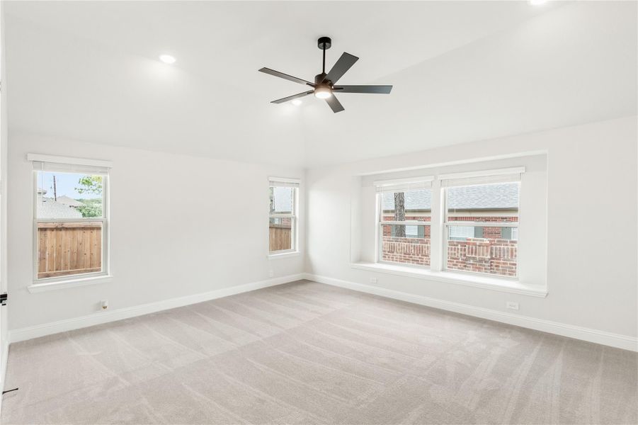 Empty bedroom with light gray carpet, ceiling fan, and multiple windows with white trim