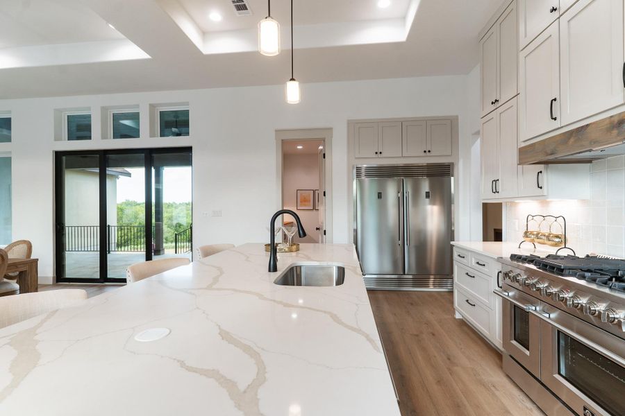 Kitchen featuring high quality appliances, decorative light fixtures, light wood-style flooring, backsplash, and a raised ceiling Kitchen featuring high quality appliances, decorative light fixtures, light wood-style flooring, backsplash, and a raised ceiling