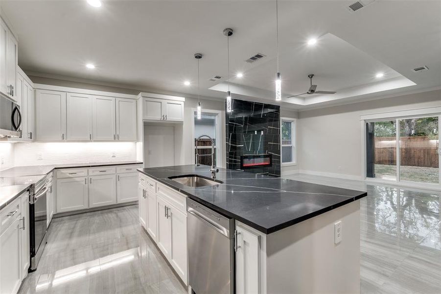 Kitchen with white cabinets, appliances with stainless steel finishes, a kitchen island with sink, sink, and decorative light fixtures