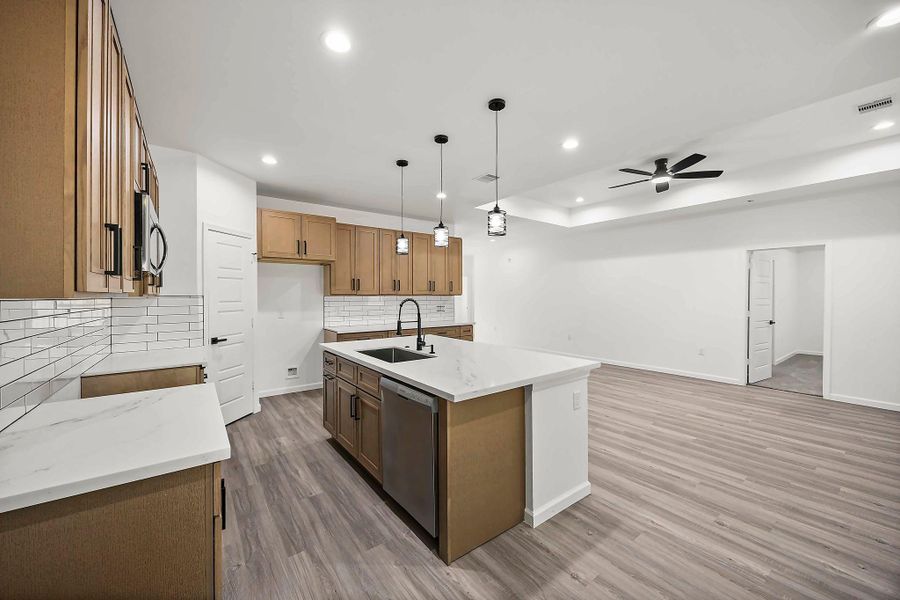 Modern open-concept kitchen with sleek wood cabinetry, a spacious island, and elegant pendant lighting, seamlessly connected to a bright living area with stylish wood like flooring and a ceiling fan.