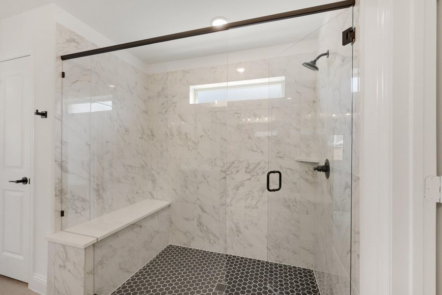 Walk-in shower with marble tile walls, glass door, built-in bench, and dark hexagon floor tile