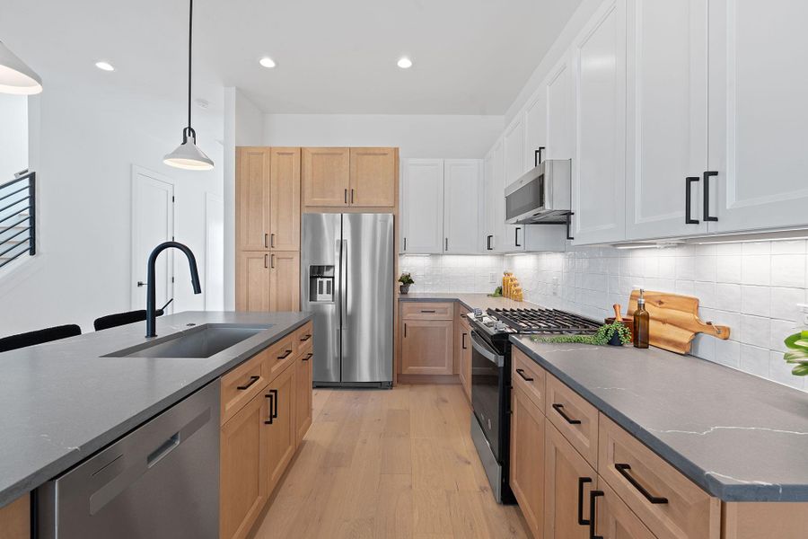 Kitchen with a sink, appliances with stainless steel finishes, light wood finished floors, decorative backsplash, and hanging light fixtures