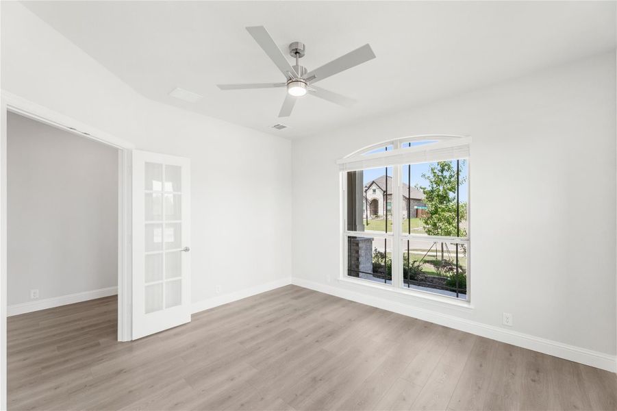 Empty room with hardwood floors, ceiling fan, arched window, and glass-panel door