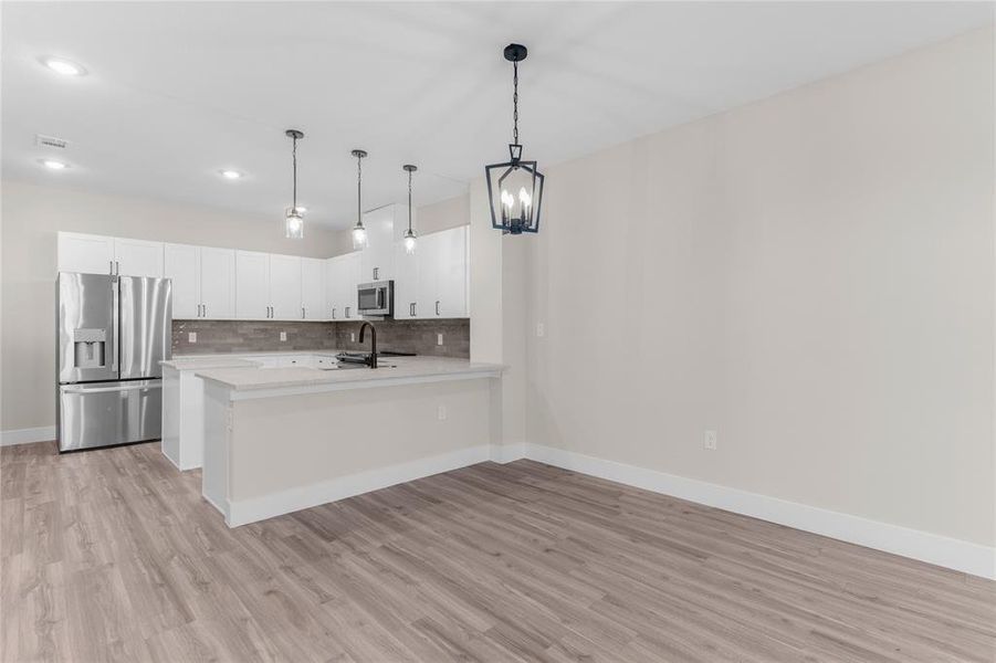 Modern kitchen and dining area featuring wood-finish flooring, white cabinetry, stainless steel appliances, and a kitchen island with pendant lighting