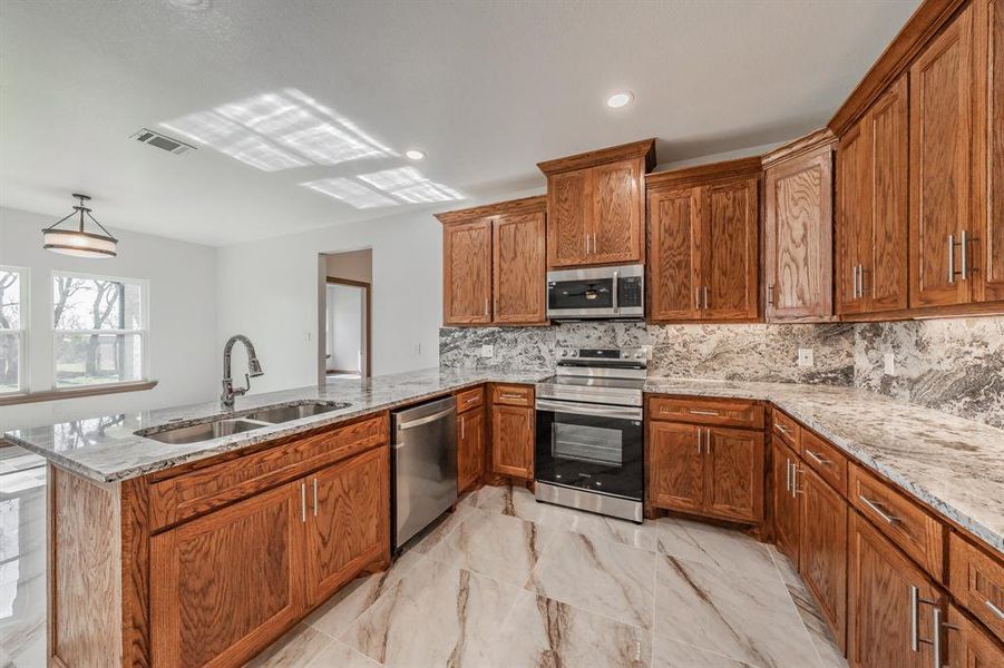 Kitchen with tasteful backsplash, appliances with stainless steel finishes, brown cabinetry, a sink, and a peninsula