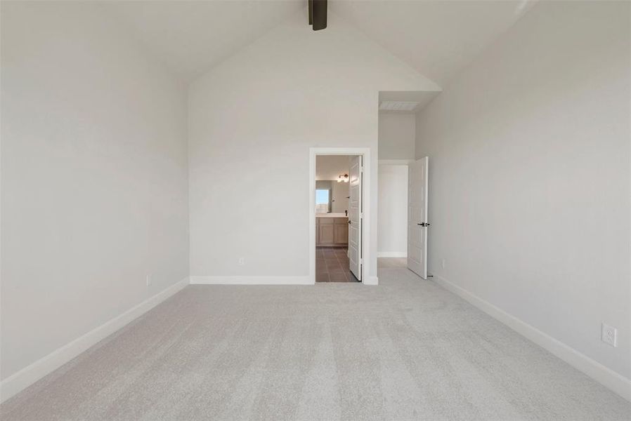 Spacious room featuring vaulted ceilings, light-colored carpeting, white baseboards, and a doorway revealing a bathroom with wood-finish flooring and a double vanity