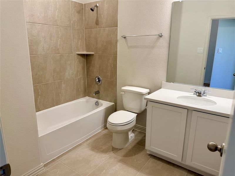 Bathroom featuring a white vanity with an integrated sink and chrome faucet, a white toilet, and a bathtub with a tiled surround