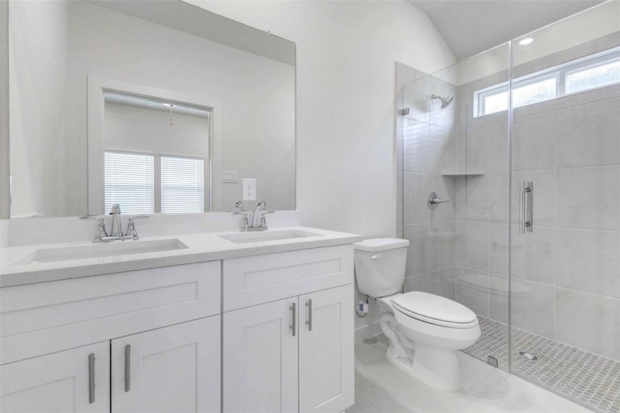 The bathroom features a bright double vanity with white cabinetry, sleek countertops, chrome fixtures, and a large mirror. A glass-enclosed shower with neutral tile, built-in niche, and modern finishes adds a clean, spa-like feel, making this space both stylish and practical. The bathroom features a bright double vanity with white cabinetry, sleek countertops, chrome fixtures, and a large mirror. A glass-enclosed shower with neutral tile, built-in niche, and modern finishes adds a clean, spa-like feel, making this space both stylish and practical.