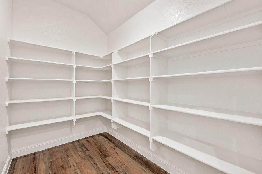 Walk-in pantry with white built-in shelves on three walls and hardwood floors