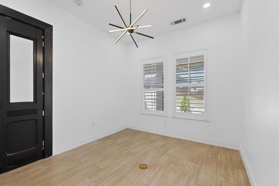 Bright room featuring wood-finish flooring, a modern linear chandelier, and two windows with white plantation shutters Bright room featuring wood-finish flooring, a modern linear chandelier, and two windows with white plantation shutters