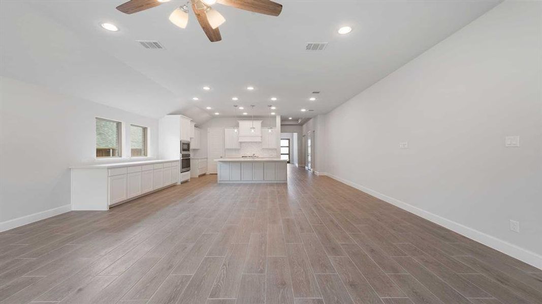 Unfurnished living room with lofted ceiling, sink, ceiling fan, and light hardwood / wood-style flooring