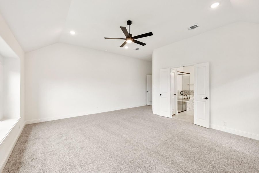 Spacious bedroom with vaulted ceiling, ceiling fan, carpet flooring, and open ensuite bathroom door