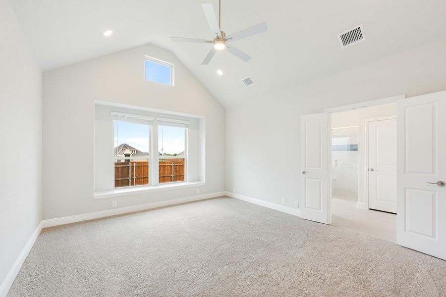 Empty bedroom with vaulted ceiling, ceiling fan, carpet flooring, and double windows overlooking backyard fence