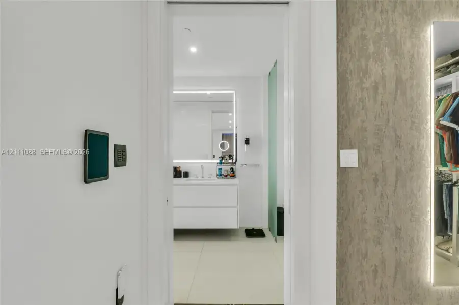 Floating white vanity with integrated lighting, oversized backlit mirror, large-format tile flooring, textured wall finish, and full-length edge-lit mirror panel Floating white vanity with integrated lighting, oversized backlit mirror, large-format tile flooring, textured wall finish, and full-length edge-lit mirror panel