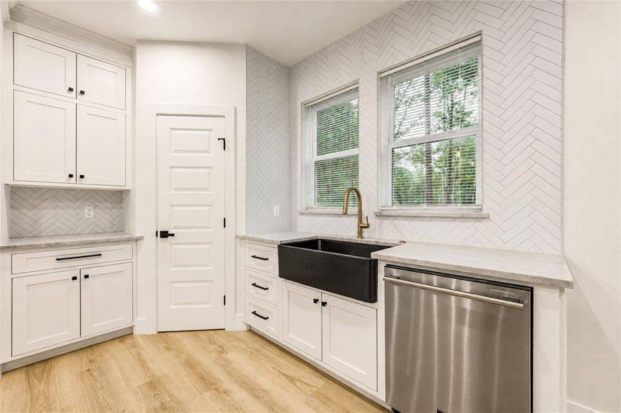Elegant kitchen featuring a farmhouse sink, stainless steel dishwasher, and chic herringbone backsplash, complemented by crisp white cabinetry.