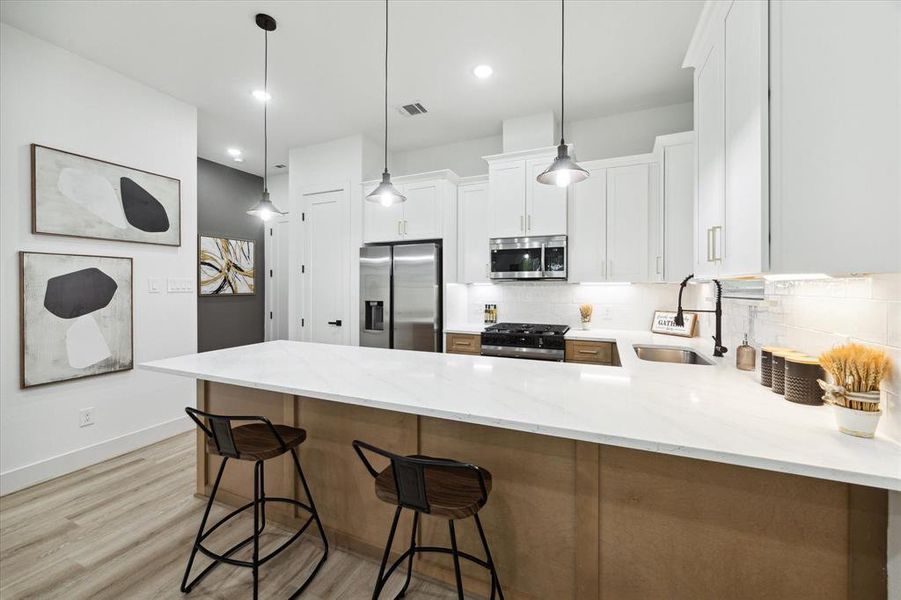 The kitchen boasts a spacious breakfast bar with seating for four, ample storage, and elegant pendant lighting. A discreetly positioned half-bath is conveniently located just off the kitchen, offering easy access for residents and guests while remaining out of sight