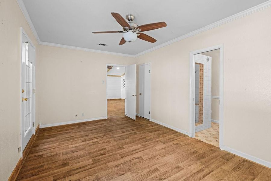 Primary bedroom with crown molding, wood finished floors, and ceiling fan