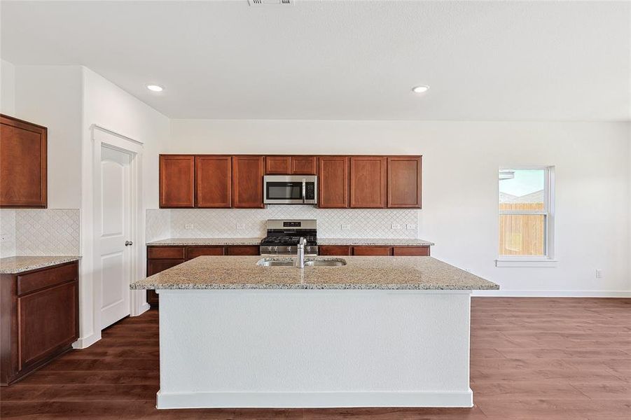 Kitchen featuring an island with sink, light stone counters, stainless steel appliances, dark wood-style flooring, and recessed lighting