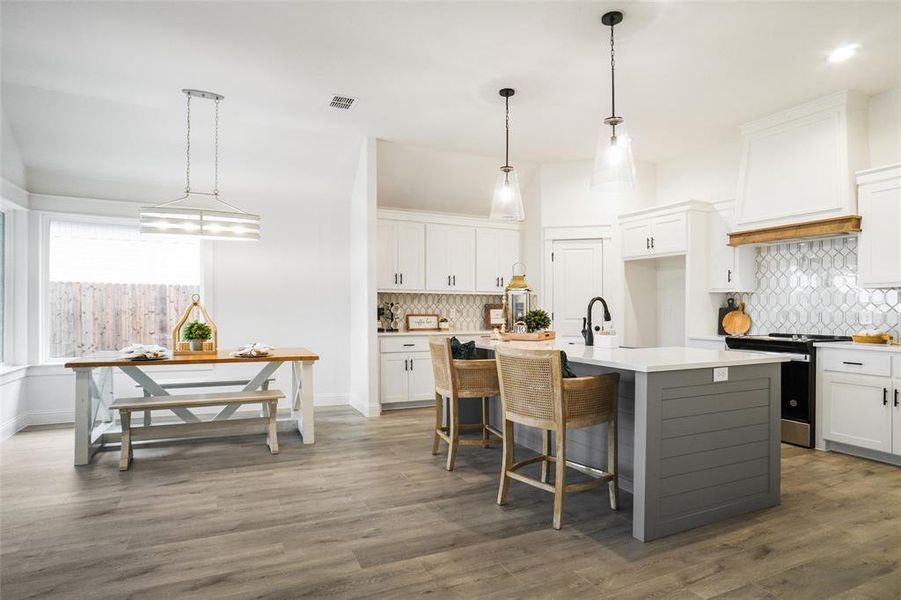 Kitchen with a kitchen island with sink, stainless steel range, and white cabinetry