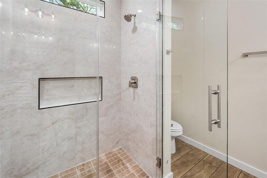 Glass-enclosed shower featuring large format tile walls, a built-in shower niche with dark trim, and a rain shower head Glass-enclosed shower featuring large format tile walls, a built-in shower niche with dark trim, and a rain shower head