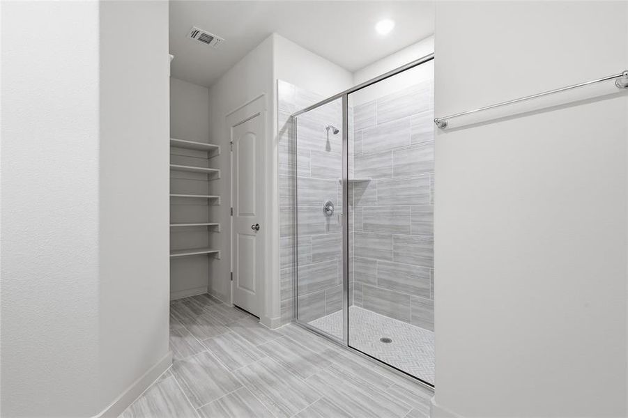 Walk-in shower featuring a glass enclosure, light-toned tile surround, and a built-in shower niche
