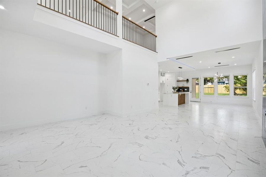 Unfurnished living room featuring light marble finish flooring, recessed lighting, a high ceiling, and a chandelier
