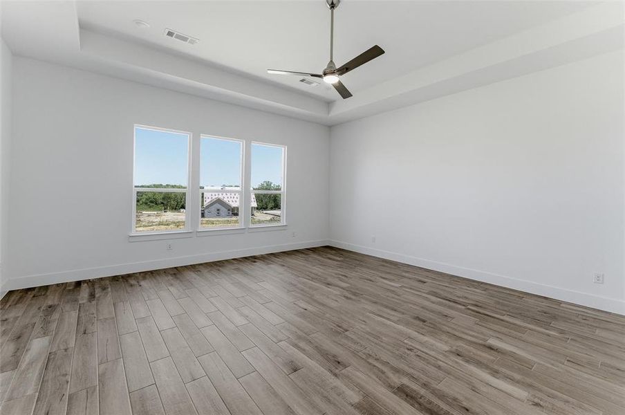 Spacious interior room featuring three large windows, wood-finish flooring, a contemporary ceiling fan, and a tray ceiling