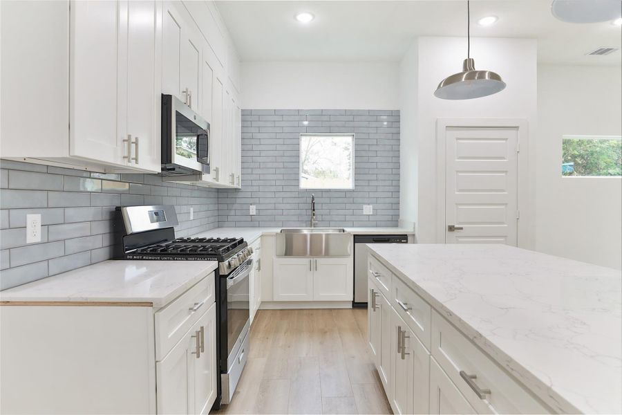 Modern kitchen with white shaker cabinetry, a spacious quartz island, and stainless steel Samsung appliances. Features sleek gray subway tile backsplash, pendant lighting, and ample natural light. Modern kitchen with white shaker cabinetry, a spacious quartz island, and stainless steel Samsung appliances. Features sleek gray subway tile backsplash, pendant lighting, and ample natural light.