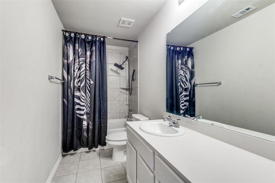 Full bathroom with shower / bathtub combination with curtain, tile patterned floors, a textured ceiling, toilet, and vanity