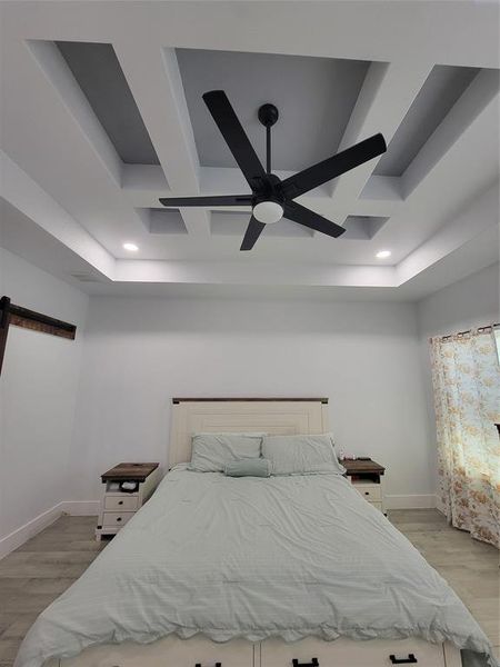 Primary 
Bedroom with a barn door, light wood-type flooring, coffered ceiling, a tray ceiling, and recessed lighting