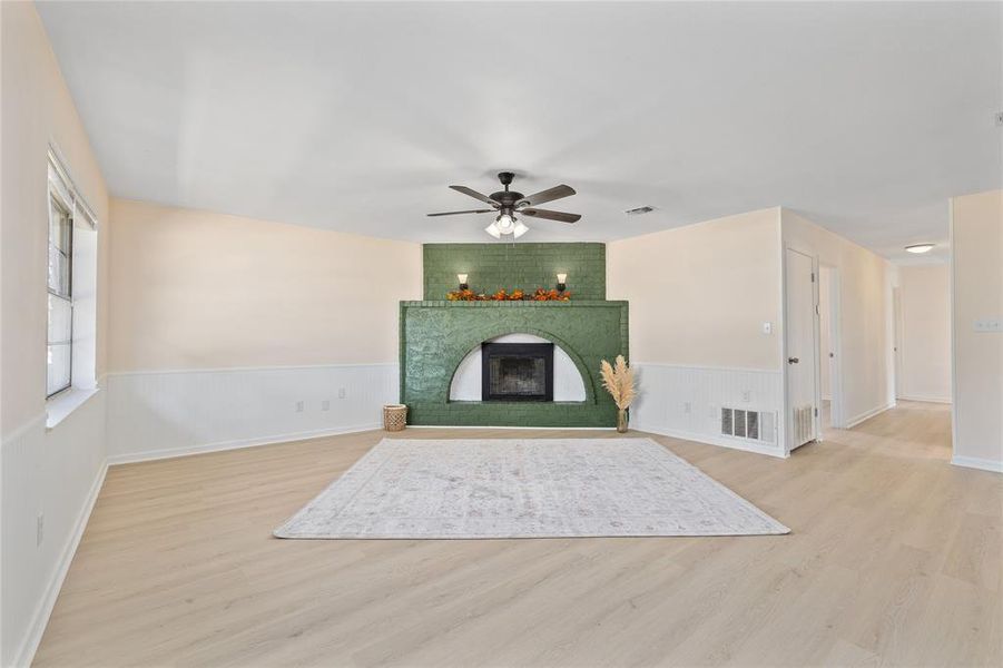 Unfurnished living room featuring a fireplace, light wood-type flooring, a wainscoted wall, and ceiling fan