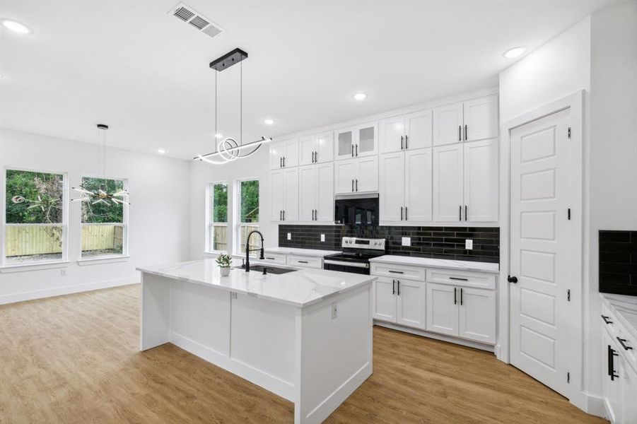 Kitchen with light wood-type flooring, an island with sink, light stone countertops, stainless steel electric range oven, and sink