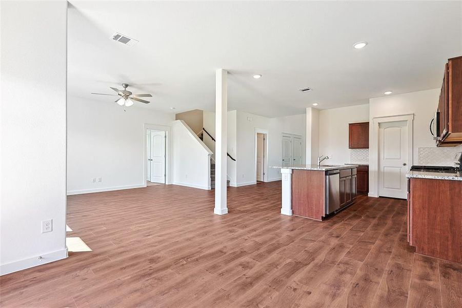 Kitchen with ceiling fan, an island with sink, tasteful backsplash, dark wood-type flooring, and stainless steel appliances