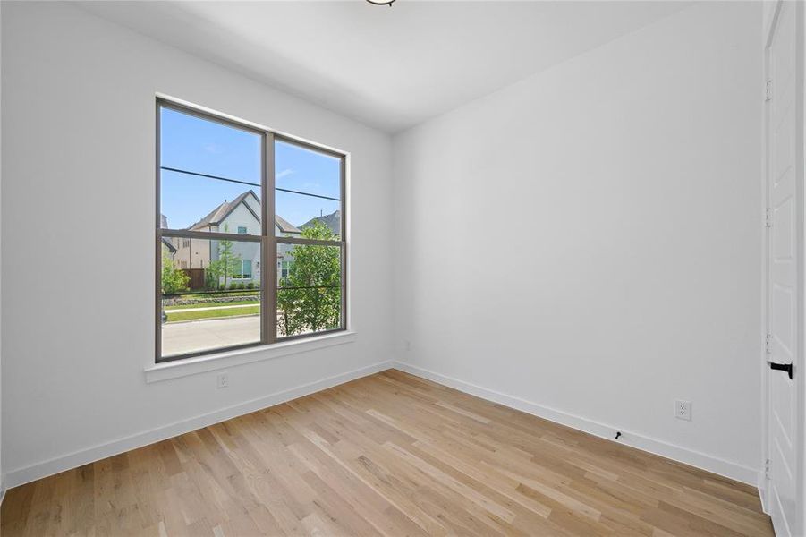 Bright interior space featuring a large window with dark trim, wood-finish flooring, white baseboards, and a white interior door with a black handle