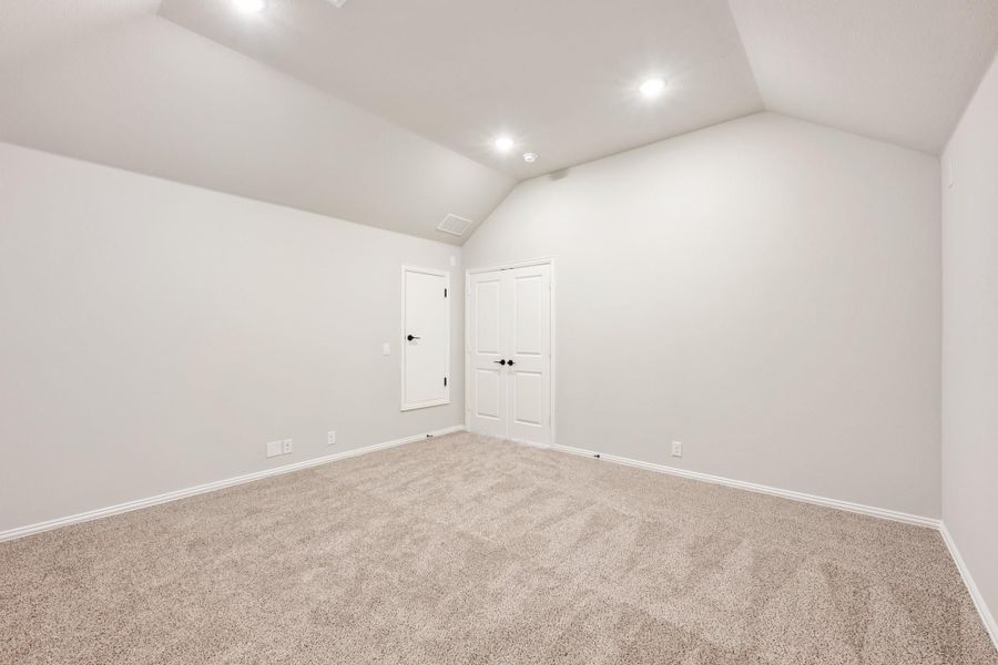 Empty bedroom with vaulted ceiling, carpet flooring, and double closet doors Empty bedroom with vaulted ceiling, carpet flooring, and double closet doors