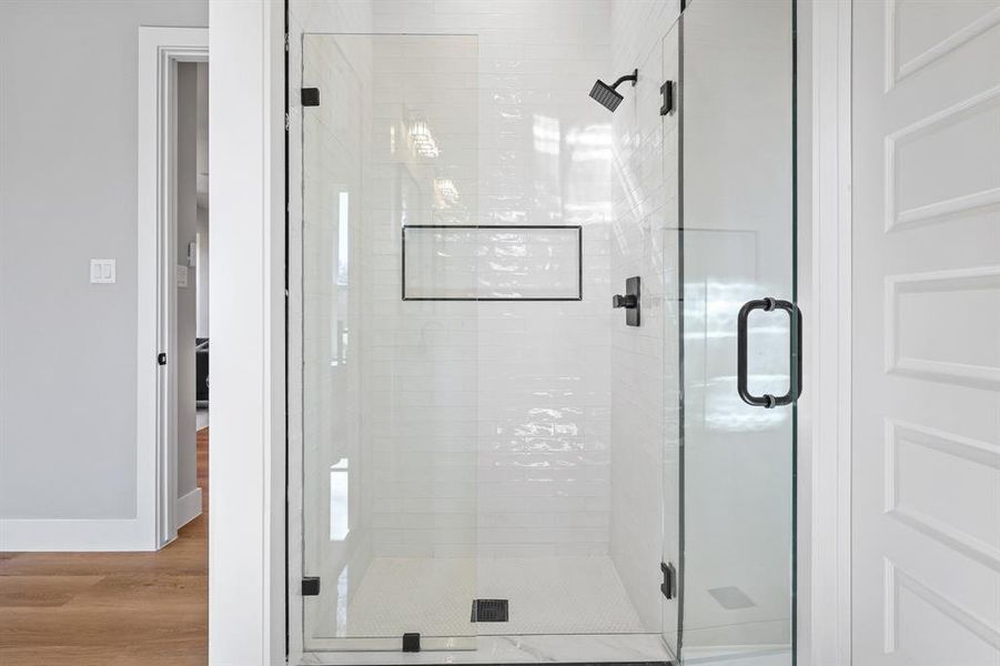 Full bath featuring a stall shower, baseboards, and wood finished floors