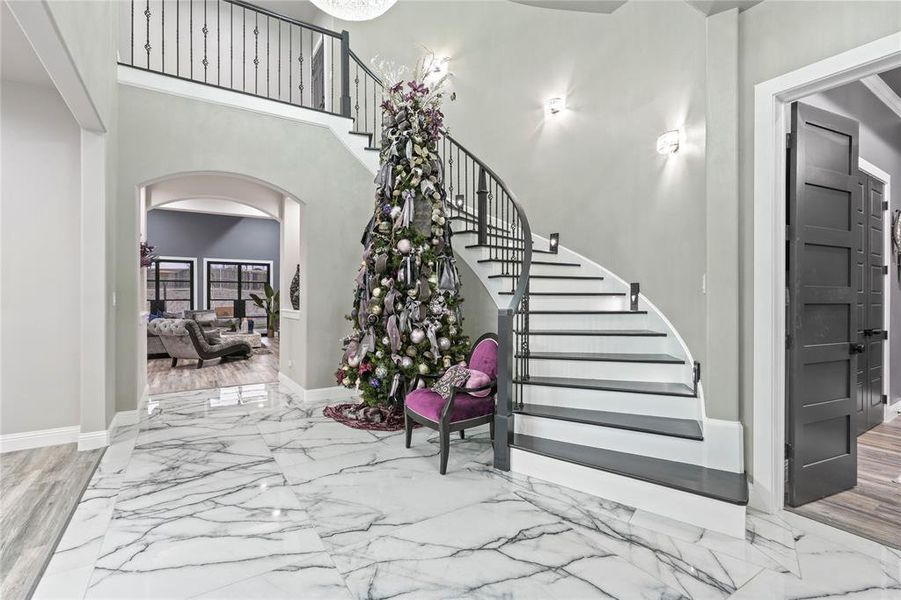 Entrance foyer featuring arched walkways, light marble finish flooring, stairs, and a high ceiling