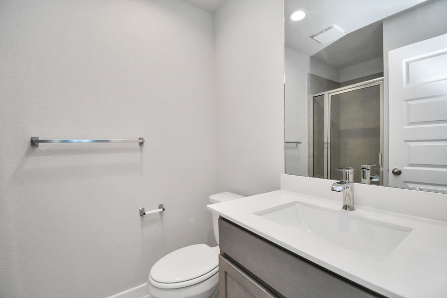 Secondary bath features tile flooring, a walk-in shower with tile surround, light stained wood cabinets, beautiful light countertop. Sample photo of completed home with similar floor plan. Actual colors and selections may vary.