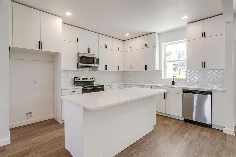 Kitchen with light hardwood / wood-style floors, a center island, sink, stainless steel appliances, and white cabinets Kitchen with light hardwood / wood-style floors, a center island, sink, stainless steel appliances, and white cabinets