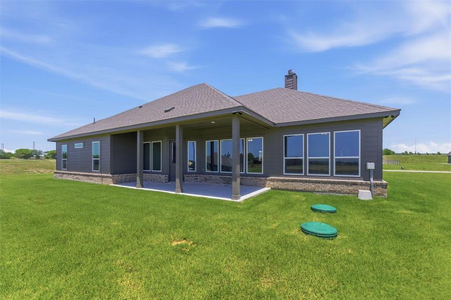 Exterior featuring dark gray siding, a covered patio with columns, a shingled roof, a brick foundation perimeter, and multiple large windows