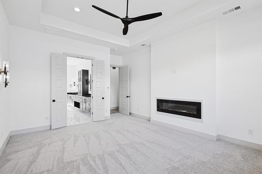 Unfurnished living room featuring ceiling fan, light carpet, and a tray ceiling