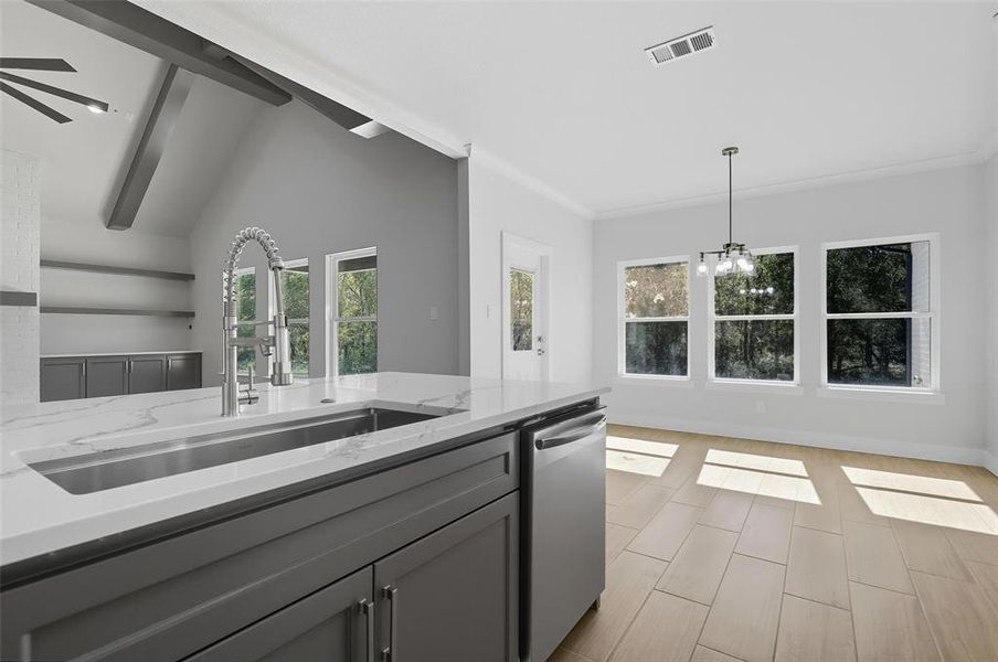 Kitchen with gray cabinets, light stone counters, stainless steel dishwasher, wood tiled floors, and decorative light fixtures Kitchen with gray cabinets, light stone counters, stainless steel dishwasher, wood tiled floors, and decorative light fixtures