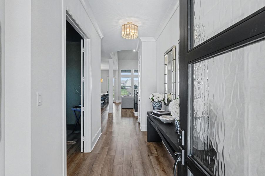 A wide gallery foyer with soaring ceilings and wide-plank flooring leads into the heart of the home. The space is accented by designer lighting and provides a clear sightline to the living areas.