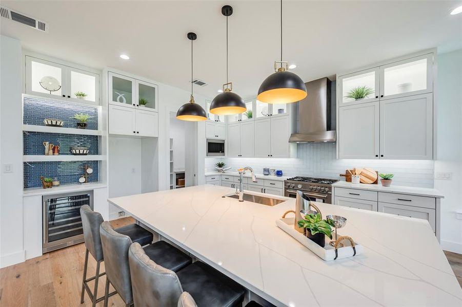 Kitchen with glass insert cabinets, light wood-style floors, decorative light fixtures, a kitchen bar, and white cabinetry Kitchen with glass insert cabinets, light wood-style floors, decorative light fixtures, a kitchen bar, and white cabinetry