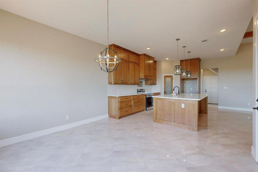 Kitchen with a center island with sink, pendant lighting, light tile patterned floors, decorative backsplash, and stainless steel range with electric stovetop