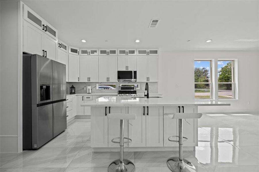 Kitchen with appliances with stainless steel finishes, a center island with sink, a kitchen breakfast bar, and white cabinets