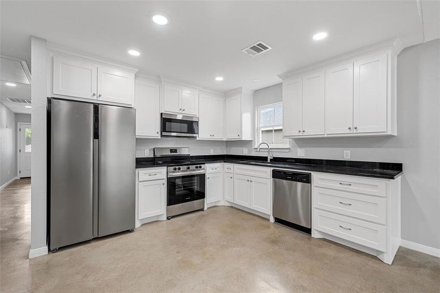 Kitchen featuring visible vents, stainless steel appliances, white cabinets, and baseboards