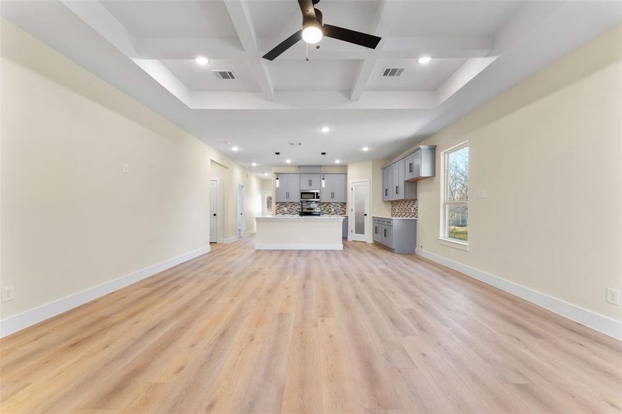 Unfurnished living room with coffered ceiling, light hardwood / wood-style flooring, beamed ceiling, and ceiling fan