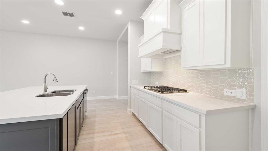 Kitchen with white cabinets, light hardwood / wood-style flooring, sink, stainless steel gas cooktop, and a kitchen island with sink