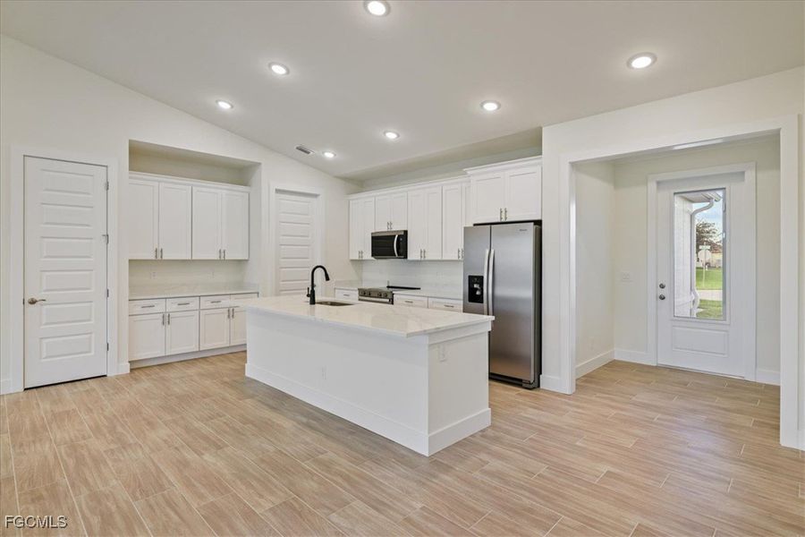 Kitchen with lofted ceiling, stainless steel appliances, white cabinets, a center island with sink, and wood finish floors